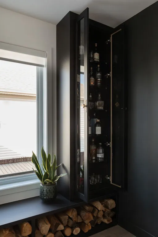Rangement noir sur mesure aux portes vitrées, bûches empilées sous la banquette près de la fenêtre