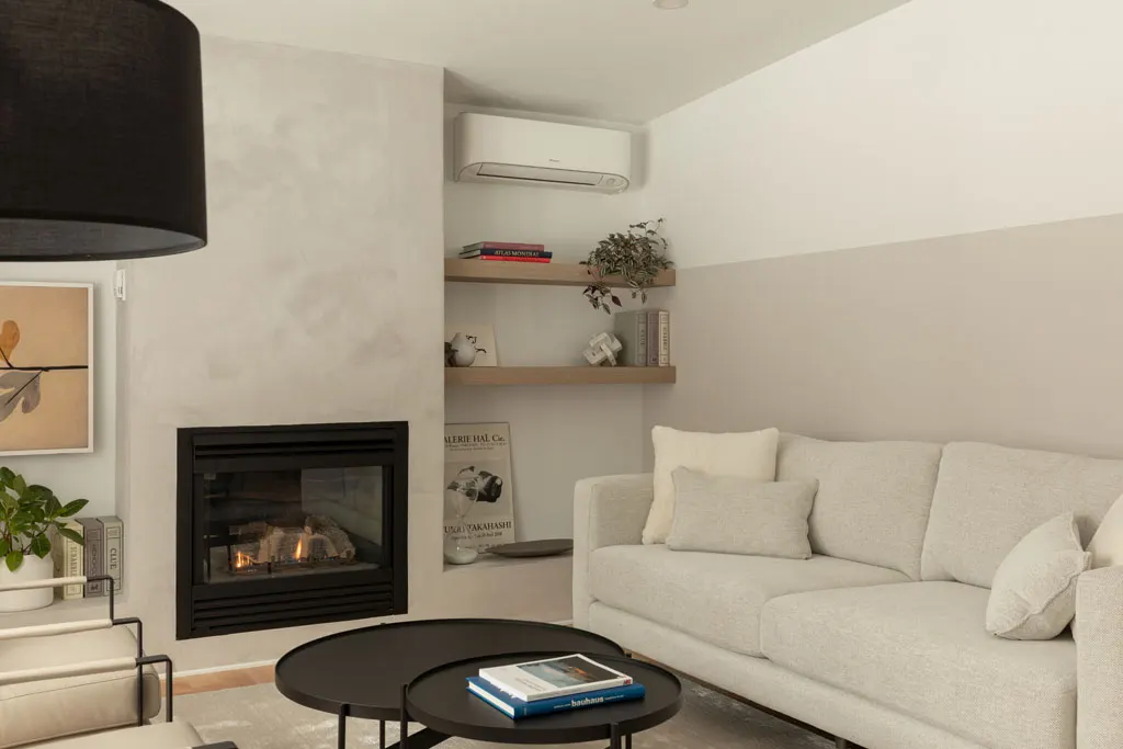 Plan rapproché du salon : foyer au gaz, thermopompe murale et grand lampadaire à abat-jour noir